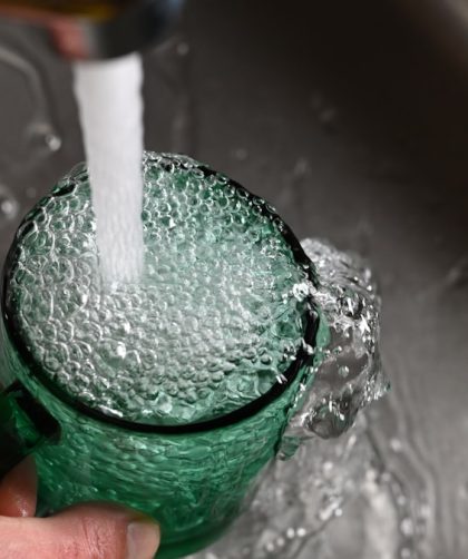 a person's hand is holding a green cup with water coming out of it